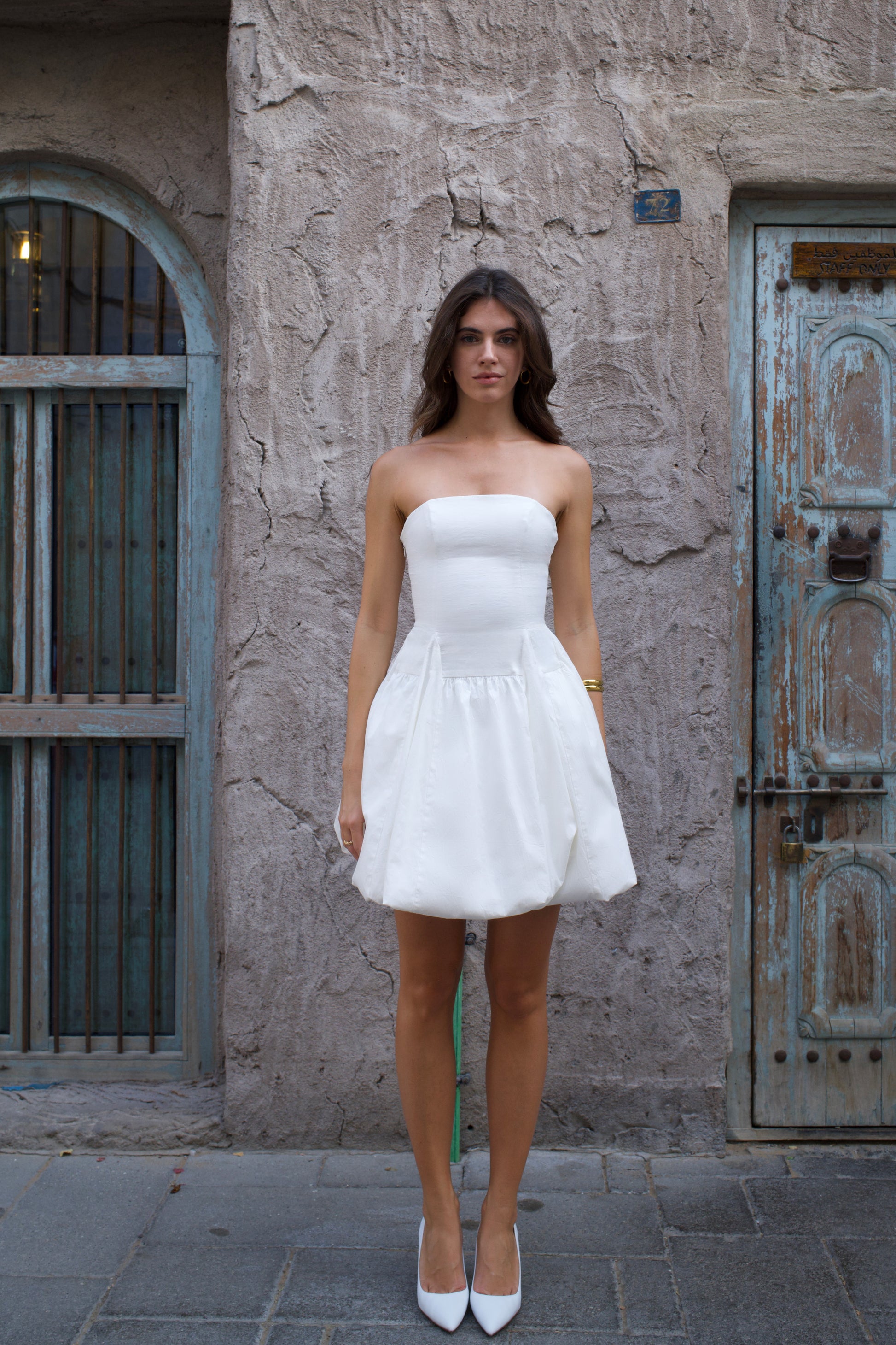 Woman in a white strapless dress standing against a textured wall with a rustic door.